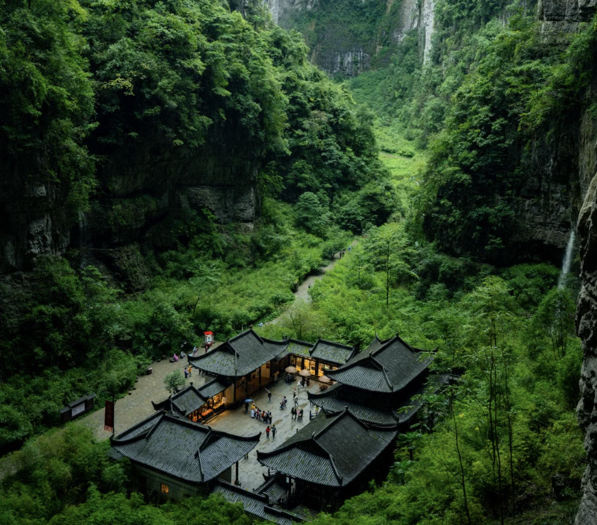 Traditional Chinese buildings nestled in a lush green karst gorge in Wulong, Chongqing, China.